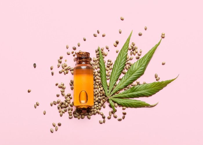 bottle of cbd oil with hemp seeds in a pink background
