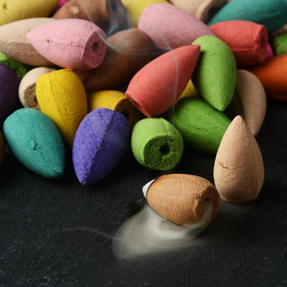 Colorful incense cones with one burning and releasing smoke on a dark surface