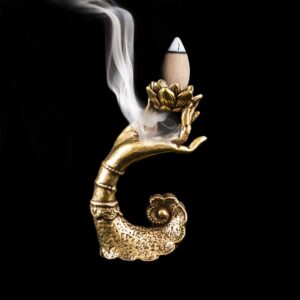 A golden hand-shaped incense holder with a burning backflow cone releasing smoke, set against a black background