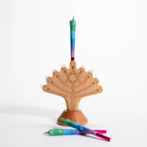Wooden menorah with Star of David design holding a colorful rainbow-wrapped candle, with additional candles placed beside it.