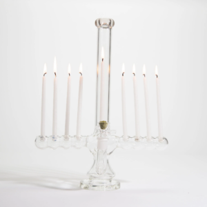 A unique clear glass menorah with lit white candles and a central bowl filled with green herb