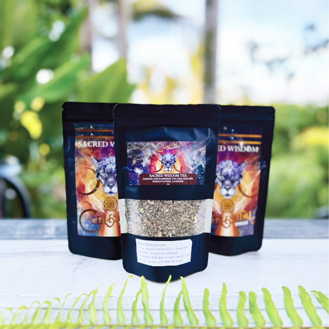 Three pouches of Sacred Wisdom Tea with vibrant cosmic-themed labels displayed outdoors on a wooden surface