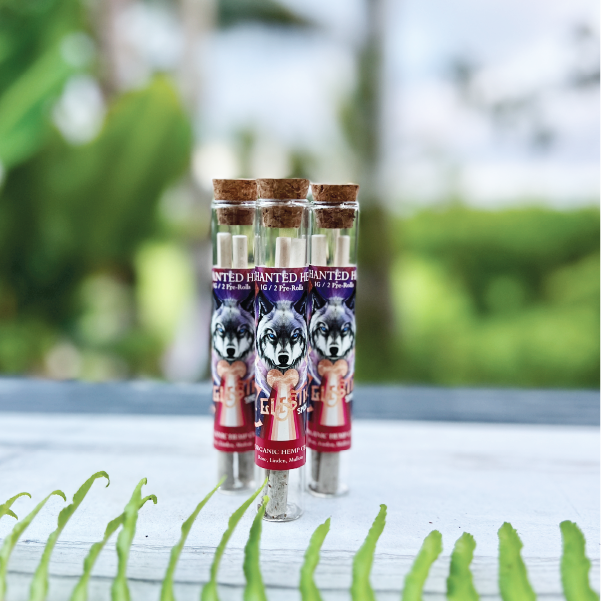 Three glass tubes with cork tops, each containing pre-rolled cones with a wolf illustration on the label, set on a white surface with green foliage in the foreground.