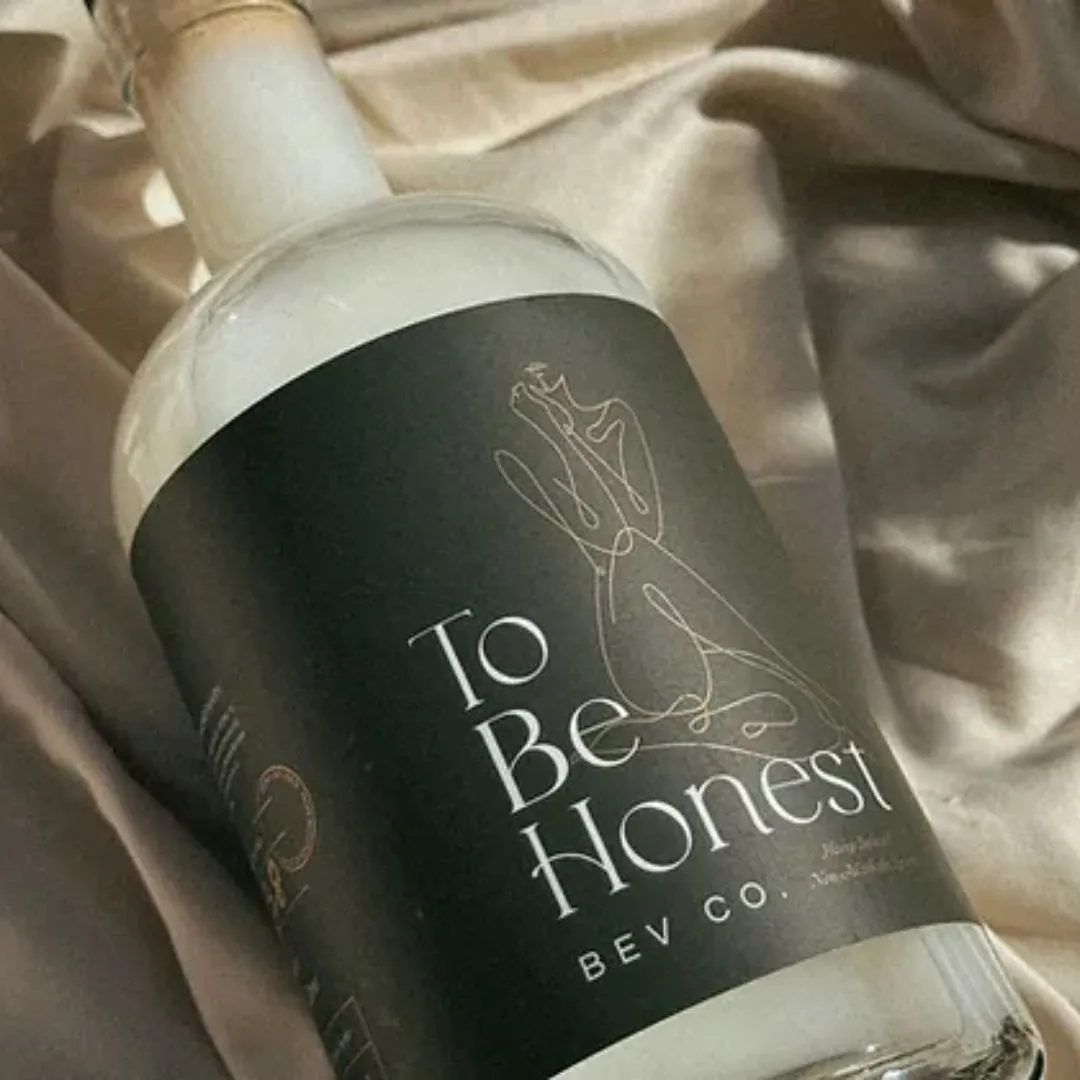 Frosted glass bottle with a black label featuring minimalist line art, resting on a beige satin fabric