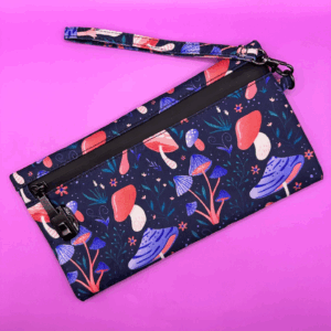 Navy blue wristlet pouch with colorful mushroom and floral pattern on a pink background