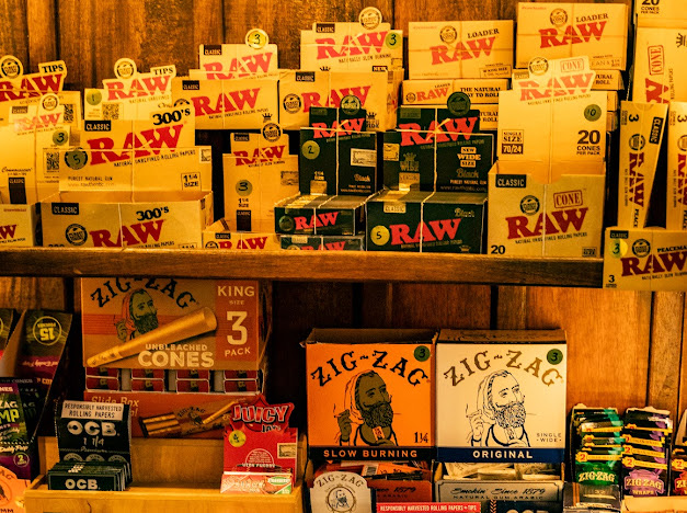 Amber-lit wood shelves displaying rolling papers and accessories at The Other Path CBD.