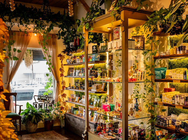 Inside The Other Path CBD, with warmly lit gold shelving, plants, cream flowers and apothecary products.